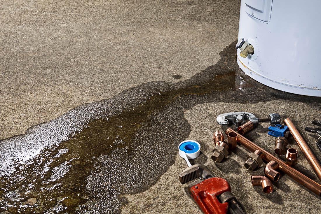 A leaking faucet on a domestic water heater with tools and fittings to replace water heater